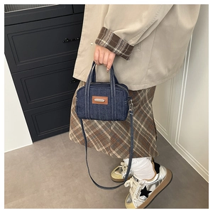 Detail view of mini denim crossbody bag with brown leather patch and dual handles