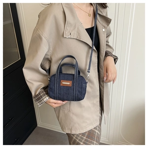 Detail of blue denim pillow bag with white contrast stitching and leather tag on a model
