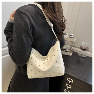 Detail of white glossy leather bucket bag featuring silver stud rivets and a shoulder strap