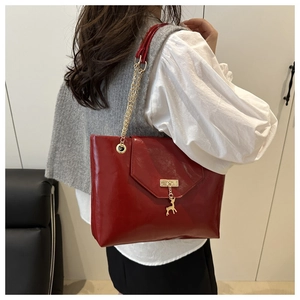 Detail of red patent leather tote bag with gold chain strap and deer pendant charm
