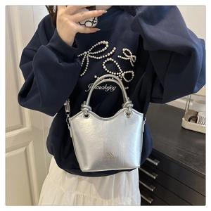 Detail of silver metallic bucket bag with dual handles and adjustable shoulder strap