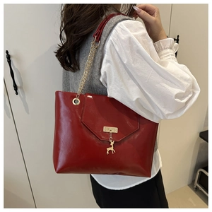 Detail of red patent leather tote bag featuring gold chain strap and deer charm