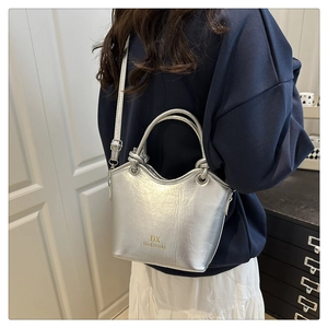 Detail view of silver bucket bag featuring knotted top handle and golden brand logo