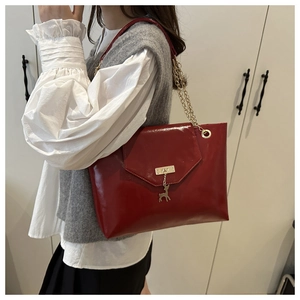 Close-up of bright red patent leather tote bag with gold deer pendant and chain strap