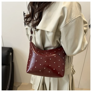 Detail of dark red leather bucket bag with silver metal studs shown on a shoulder