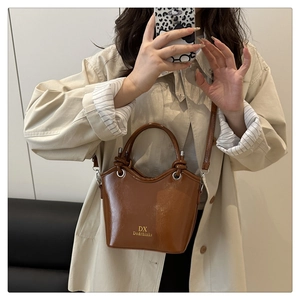 Brown leather bucket bag with gold logo shown on model wearing a beige coat