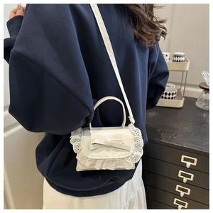 Detail of white leather crossbody bag with lace trim and bow accent on a model