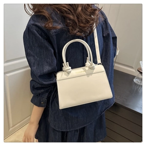 Detail of white leather handbag featuring top circular handle with decorative knot and gold text