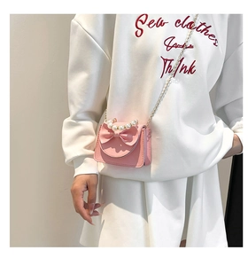 Pink mini crossbody bag with bow detail and pearl handle worn on white sweatshirt