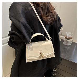 Chic off-white leather crossbody bag featuring a gold V-shaped buckle worn by a model
