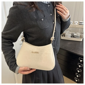 Detail of minimalist cream leather underarm bag with gold bar accent and slim strap