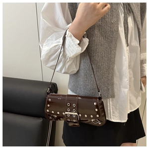 Détail du sac sous l'aisselle en cuir verni marron foncé avec rivets argentés et boucles
