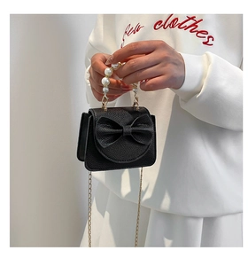 Detail view of mini black bow bag featuring large pearl handle and gold chain strap