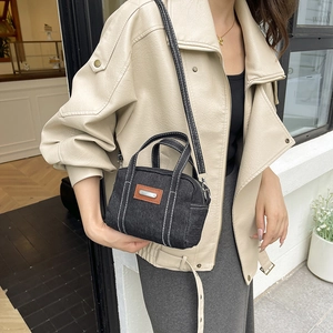 Dark blue denim crossbody pillow bag with white stitching and leather patch details