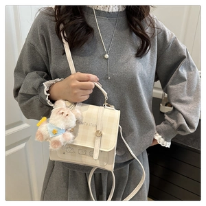 Chic cream checkered crossbody bag with plush bear charm worn by a model