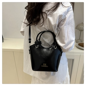 Macro detail of the black bucket bag showing shiny leather texture and golden brand logo