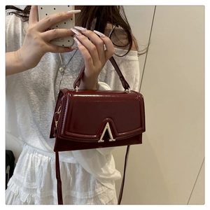 Detail of burgundy patent leather handbag with golden V-shaped buckle and crossbody strap