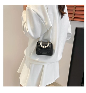 Detailed view of mini black crossbody bag with bow, pearl handle and litchi texture