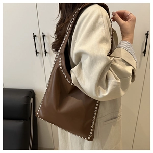 Detail of a brown leather shoulder bag with silver rivet trim shown on a model