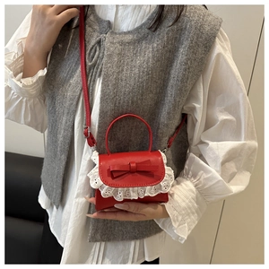 Detail of red mini handbag with white lace trim and bow worn by a model
