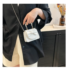 Detailed shot of white mini bag with large bow, pearl handle, and gold chain strap