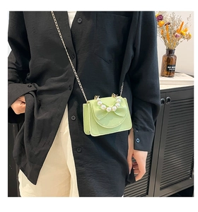 Close-up of light green crossbody bag with pearl handle and ribbon bow detail