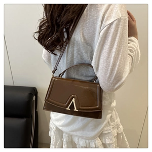 Detail of a dark brown leather crossbody bag featuring a large gold letter A buckle