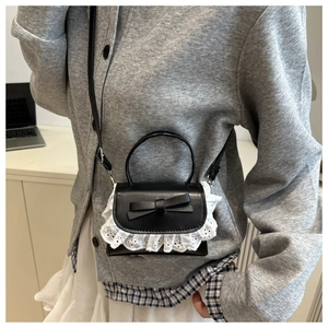 Detail of black faux leather mini bag with white lace trim and bow on front flap