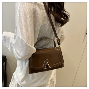 Detail of a brown leather crossbody bag featuring a gold V-shaped buckle clasp on the flap