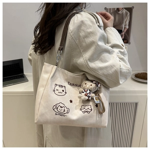 Detail of off-white canvas tote with cat print, leather strap and plush charm