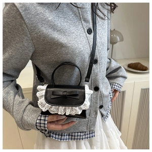Detail view of mini black crossbody bag with white lace trim and leather bow decoration