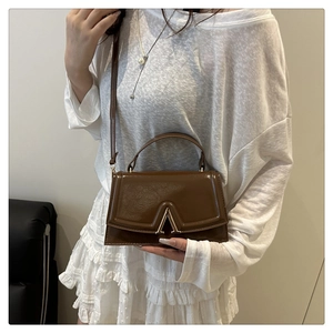 Detail view of brown leather crossbody bag with vintage V-shaped golden buckle on model