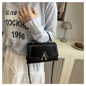 Detail of black glossy textured shoulder bag with gold V-shaped metal lock closure