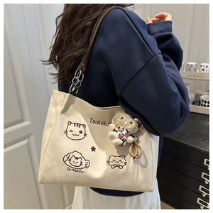 Chic cream canvas tote bag with cartoon cat print and plush pendant on model shoulder