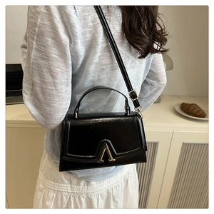 Detail of black textured leather bag with gold A-shaped buckle and crossbody strap