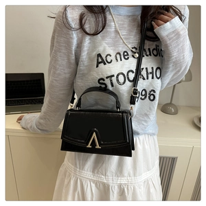 Detail of black patent leather bag featuring a gold V-shaped metal buckle and slim strap
