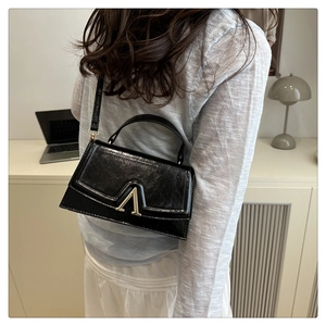 Detail of minimalist black leather handbag with gold metal clasp on model's shoulder