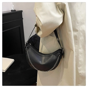 Detail of black leather half-moon crossbody bag with silver chain on model in trench coat