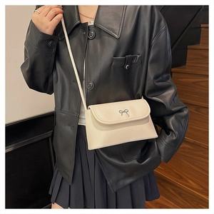 Close-up of beige PU leather crossbody bag with silver metal bow on a dark background