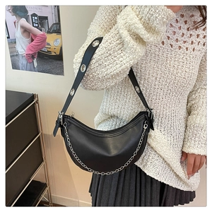 Detail of black crescent shoulder bag featuring silver metal eyelets and decorative chain