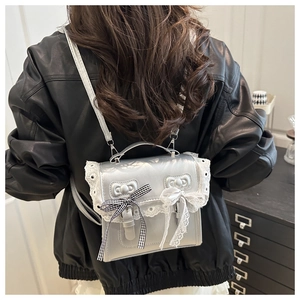 Rear view of model wearing a silver faux leather bag with white lace and bow details