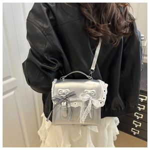 Close-up of silver crossbody bag featuring white lace trim and decorative bows