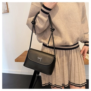 Detail of black crossbody bag featuring a silver bow metal piece and knotted shoulder strap