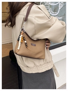 Detail of khaki canvas underarm bag with leather trim and beaded charm outdoors