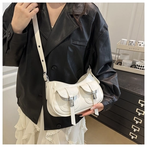 Detailed view of white crossbody bag with twin pockets and silver buckles on model