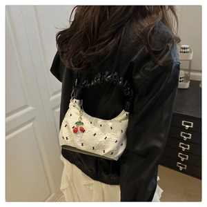 Close-up of white jacquard shoulder bag with polka dots and cherry charm accessory