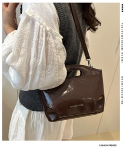 Detail of dark brown glossy shoulder bag showing silver text and shiny patent leather