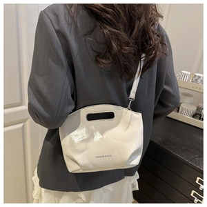Close-up of a white patent leather handbag featuring an oval cutout handle and shoulder strap