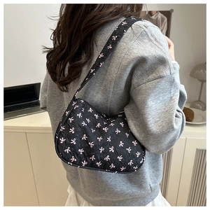 Detail of black underarm bag featuring pink bow patterns worn over the shoulder