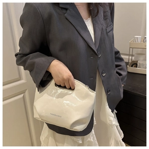 Detail of a creamy white glossy handbag with a cutout handle and stylish logo print